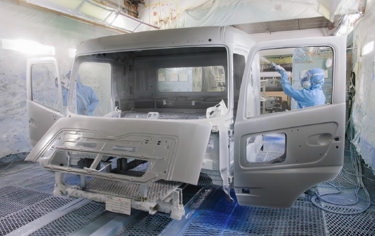 プレスや溶接で鉄板をキャビン（運転席）の形にしたりお客様の希望の色に塗装している様子の写真
