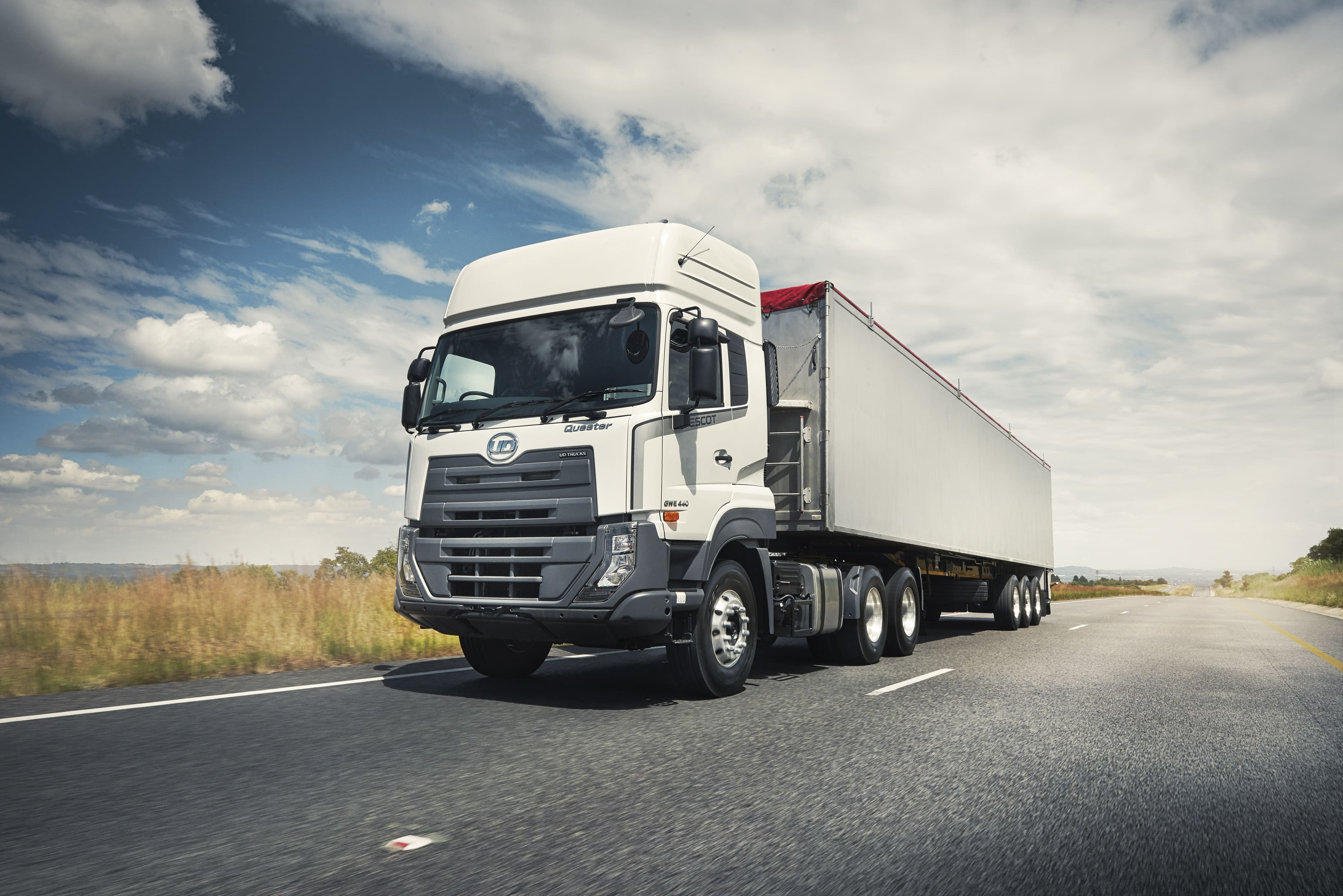 White semi-truck driving on a highway under a partly cloudy sky.