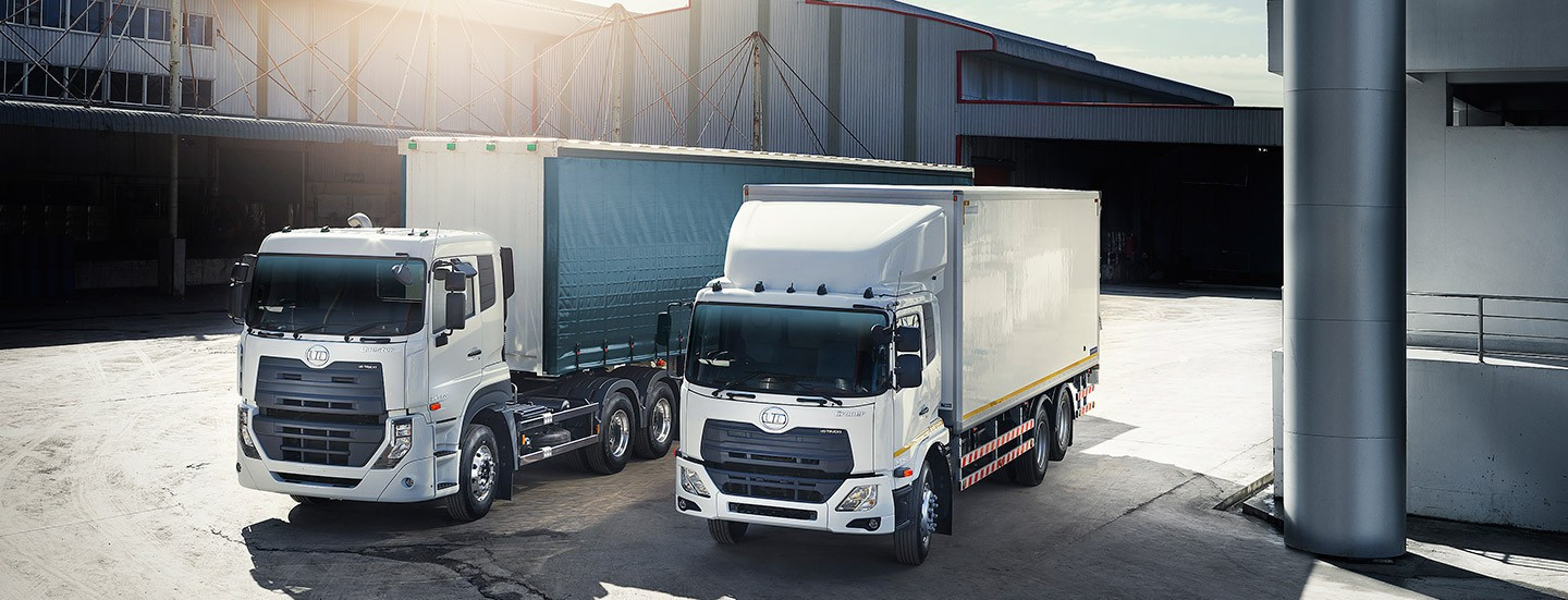 Two white cargo trucks parked outside a warehouse in daylight.