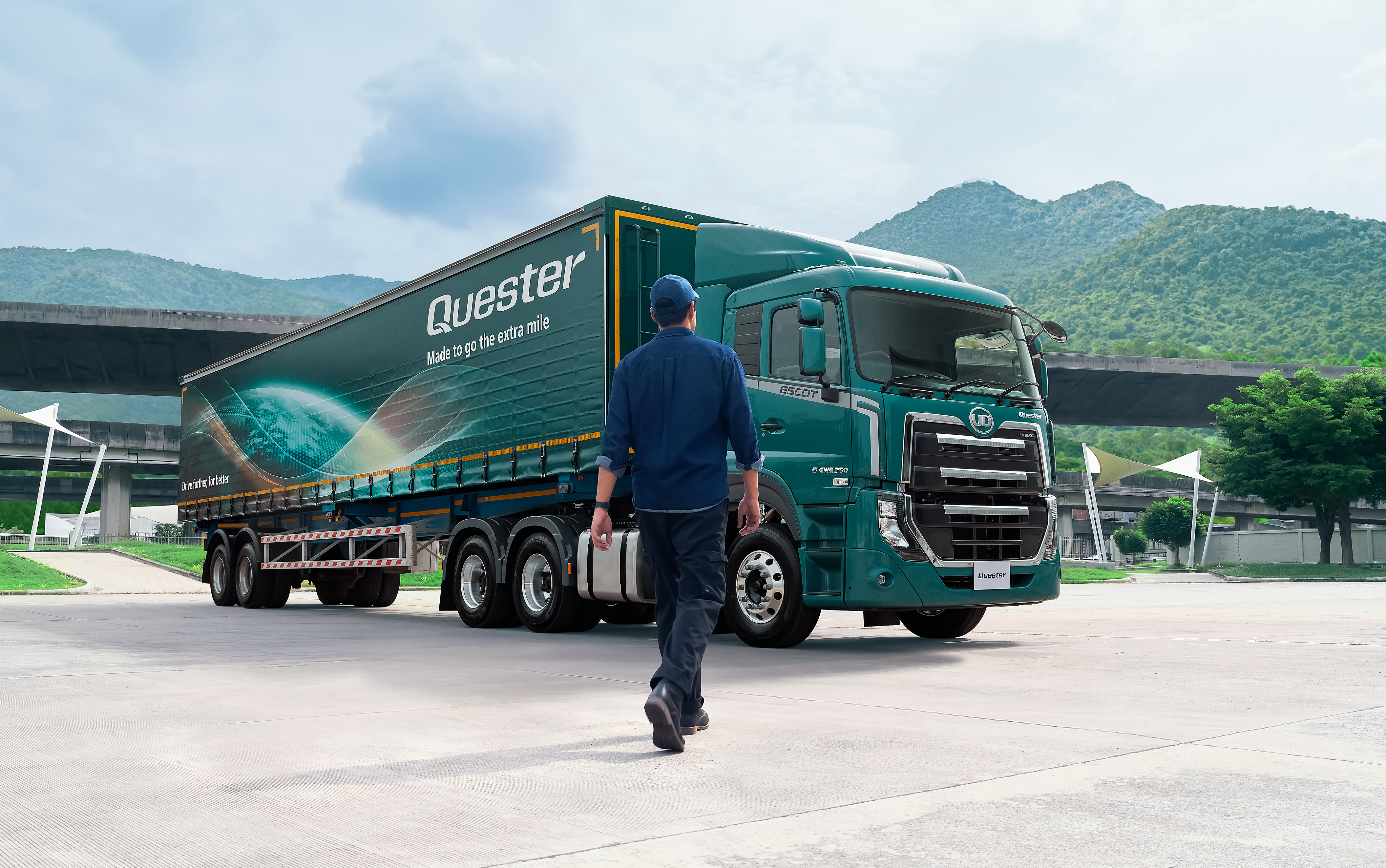 Quester Man in uniform walking toward a large green truck with mountains in the background.