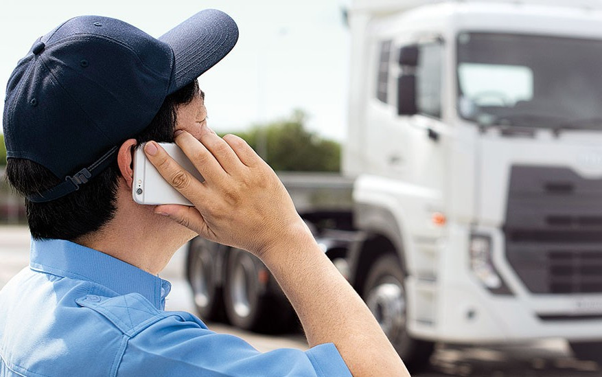 Man in blue shirt and cap talking on phone near a white truck.
