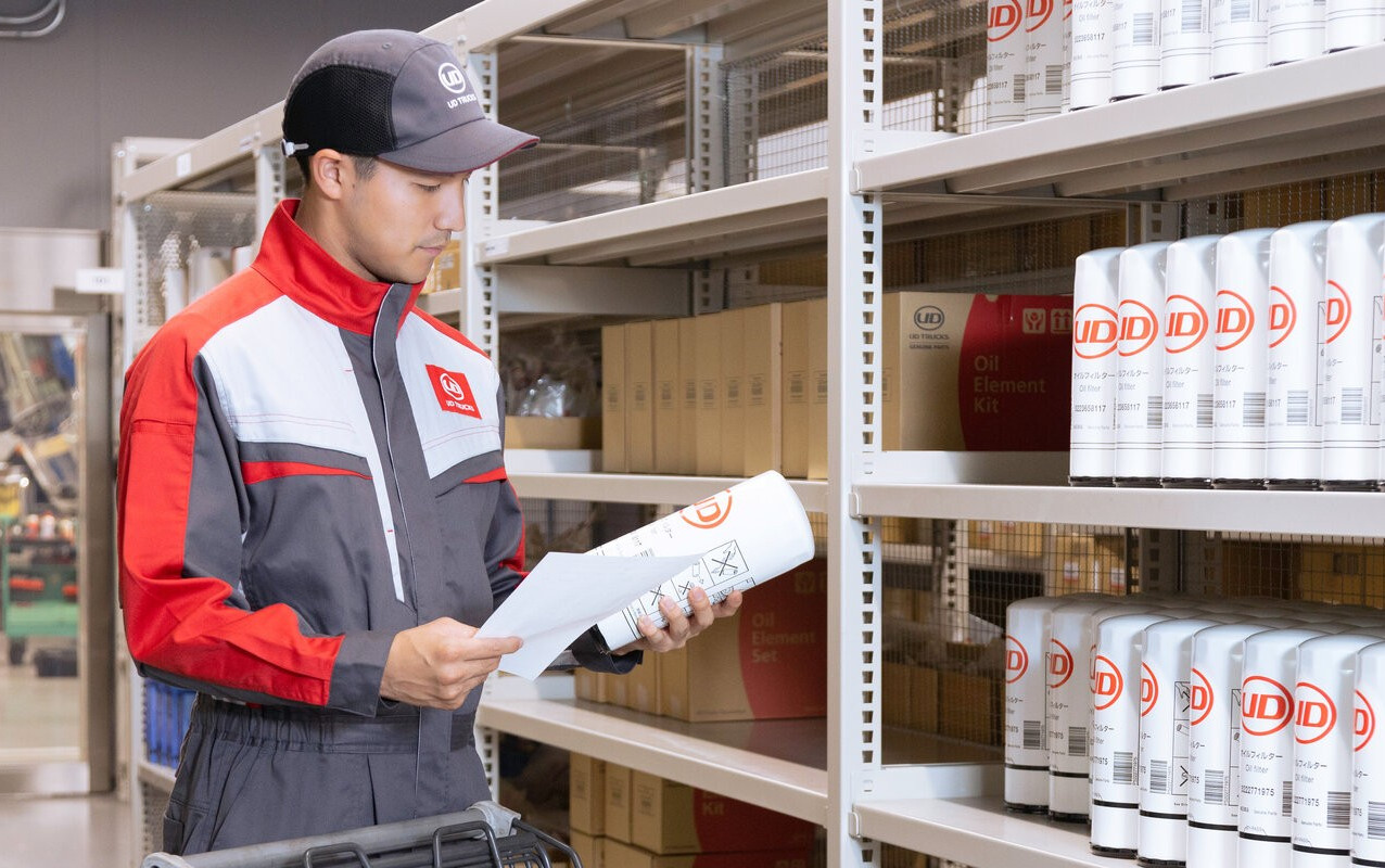 Worker in uniform checking inventory on shelves stocked with auto parts.