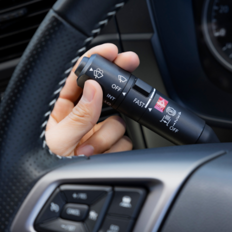 Hand adjusting a car windshield wiper control lever on the steering wheel.