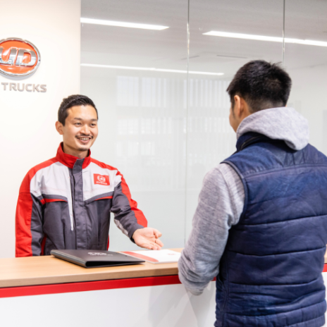 Receptionist smiling and greeting customer at a service counter.