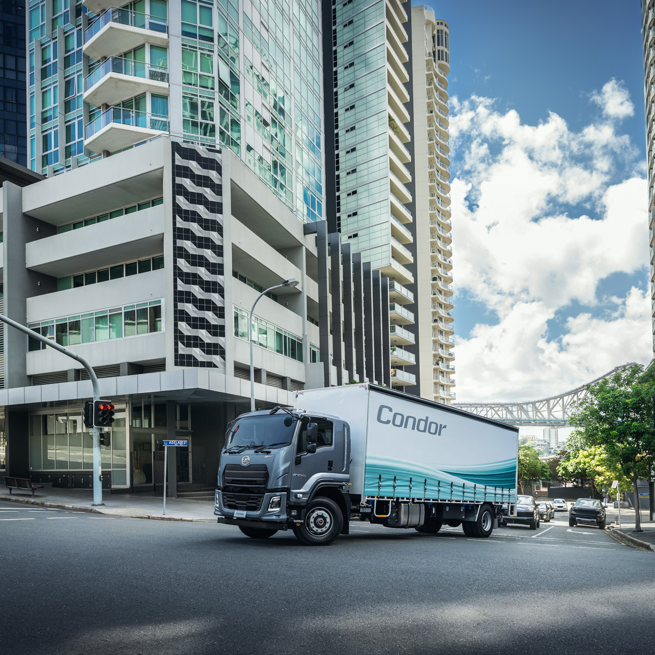 Large delivery truck turning on a city street, surrounded by tall modern buildings.