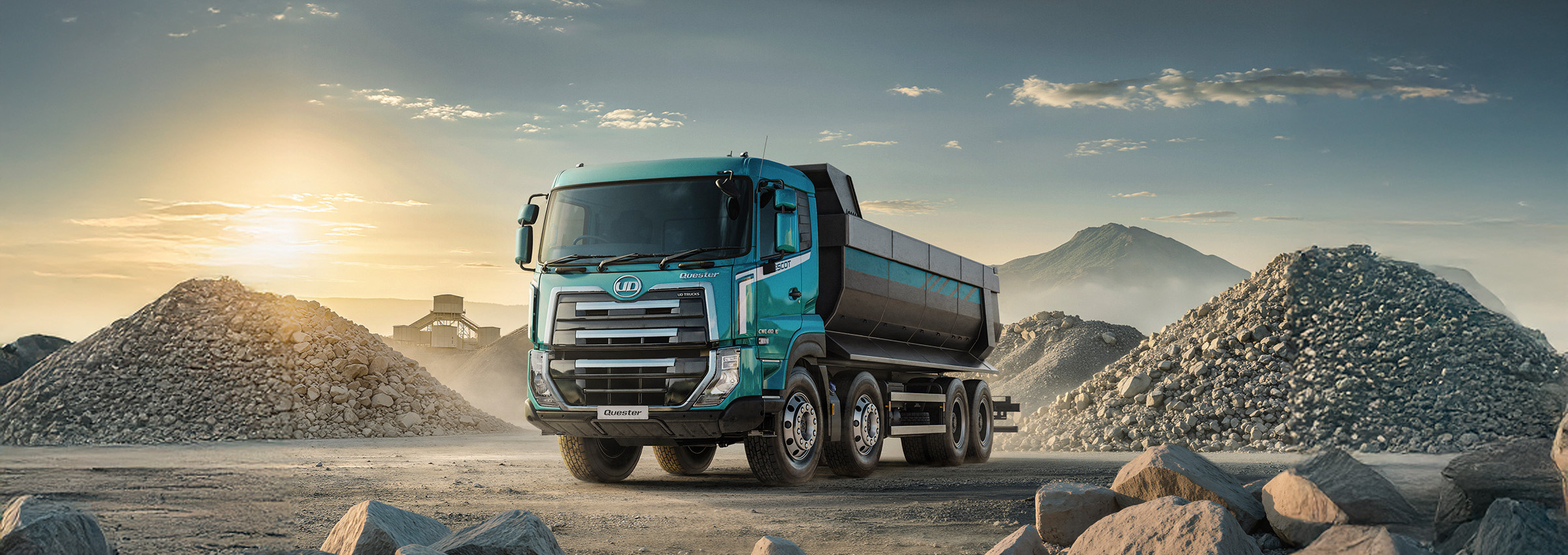 Blue dump truck on rocky construction site at sunset, gravel piles in the background.