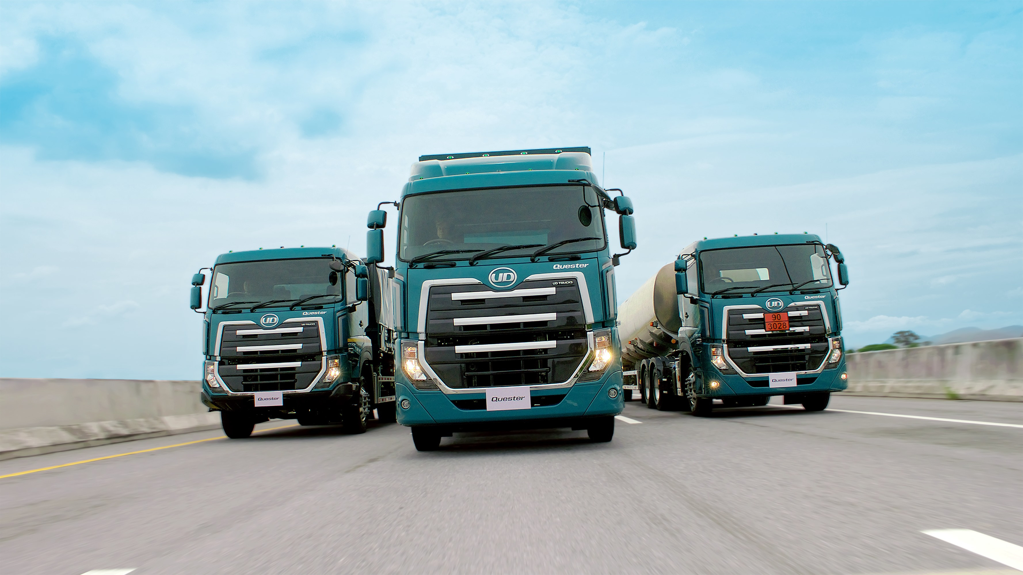 Malori matatu makubwa ya rangi ya bluu yanatembea barabarani chini ya anga yenye rangi ya samawati.