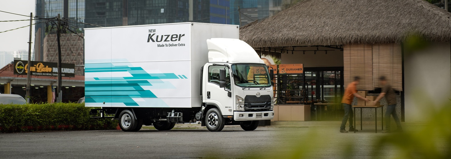 White delivery truck parked near thatched building in urban area with high-rise background.