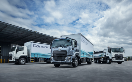 Three large blue and white trucks parked outside a warehouse under a cloudy sky.