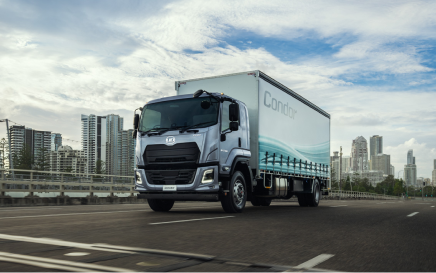 Large delivery truck driving on city road with skyscrapers in background.