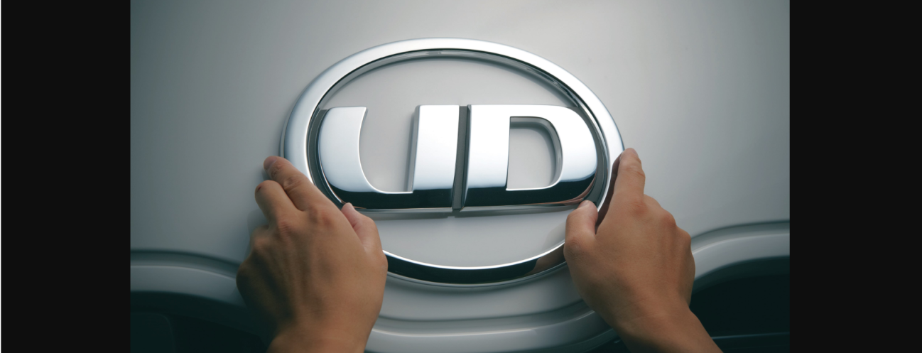 手がUDロゴのエンブレムを車のボンネットに取り付けている。