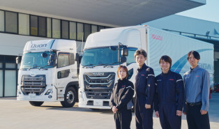 白い大型トラックの前で笑顔の作業着のスタッフ4人が並んでいる