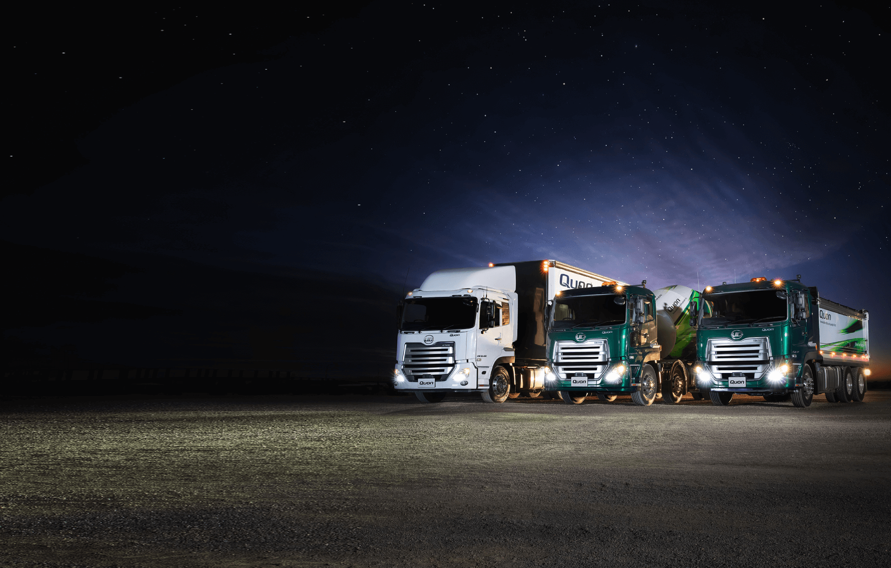Three semi-trailer trucks parked side by side at night under a starry sky.