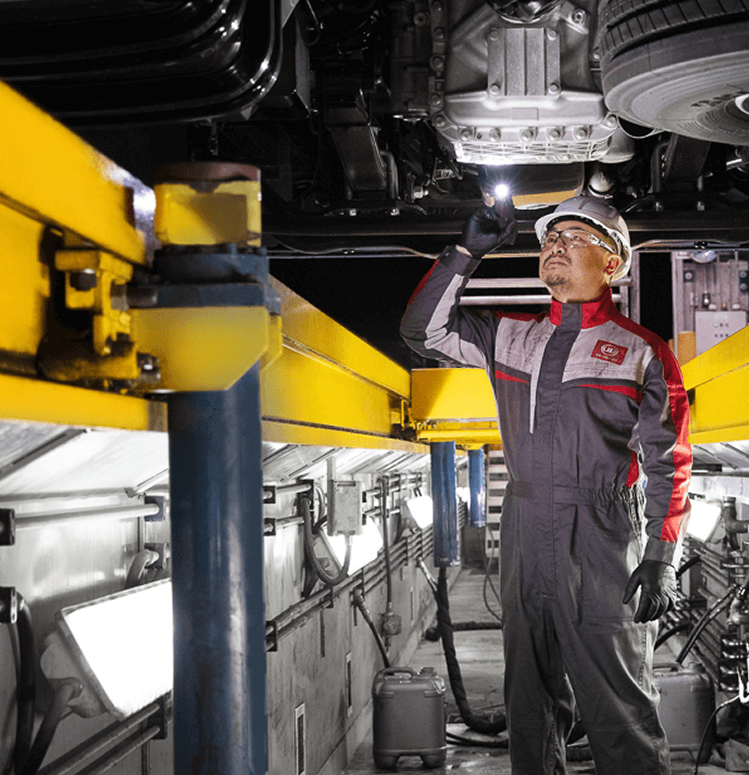 Technician inspecting vehicle undercarriage in brightly lit workshop.