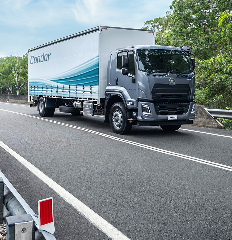 Gray delivery truck driving on a highway with green trees in the background.