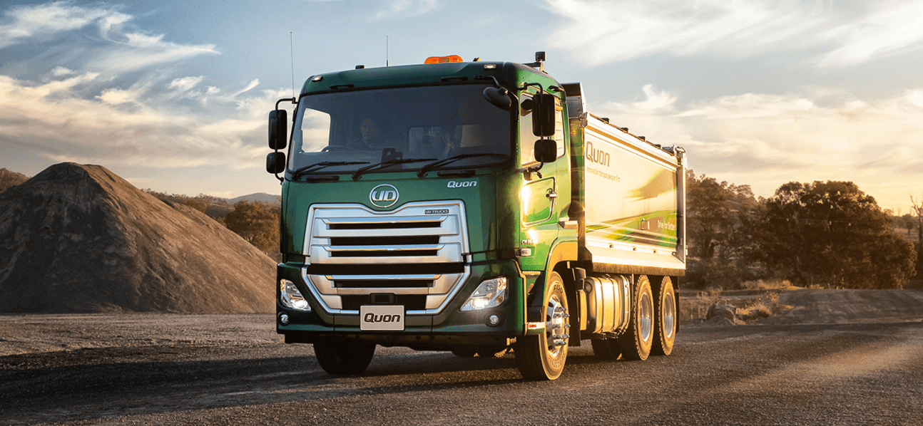Green dump truck on a gravel road at sunset with hills in the background.