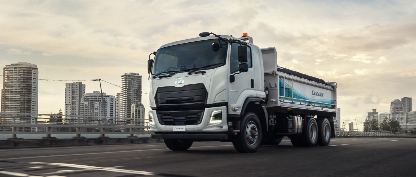 White dump truck on a city road with tall buildings in the background.